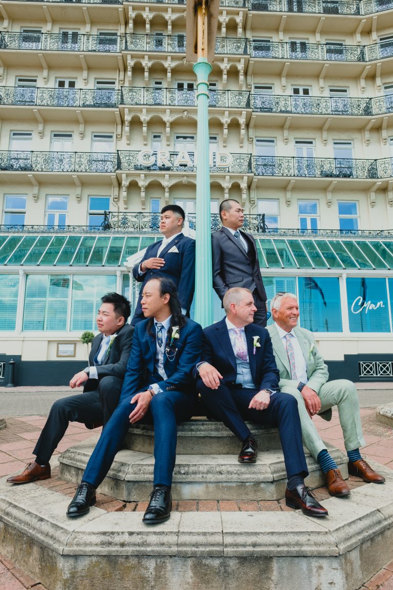 Two grooms and a group of wedding guests sitting outside the Grand Hotel